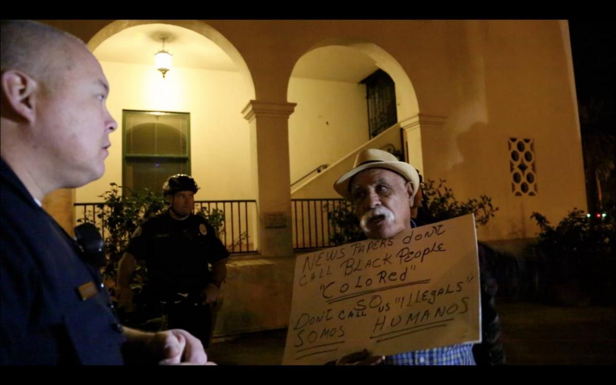 Protester with sign: "Newspapers don't call black people 'colored.' So don't call us 'illegals.' Somos humanos."